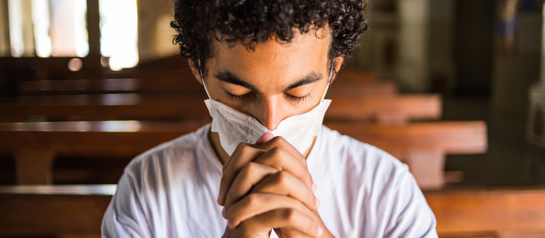 Jovem reza em igreja utilizando máscara de proteção.